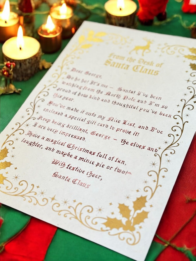 Handwritten Santa letter with gold foil design beside glowing Christmas candles and red envelope