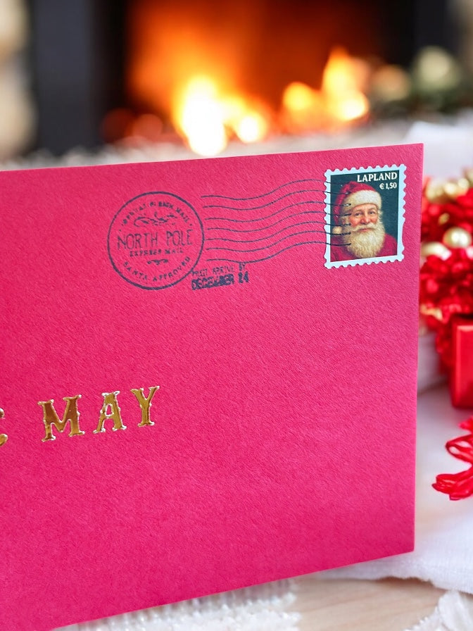 Luxury handwritten Santa letter with gold foil and red envelope beside Christmas fire